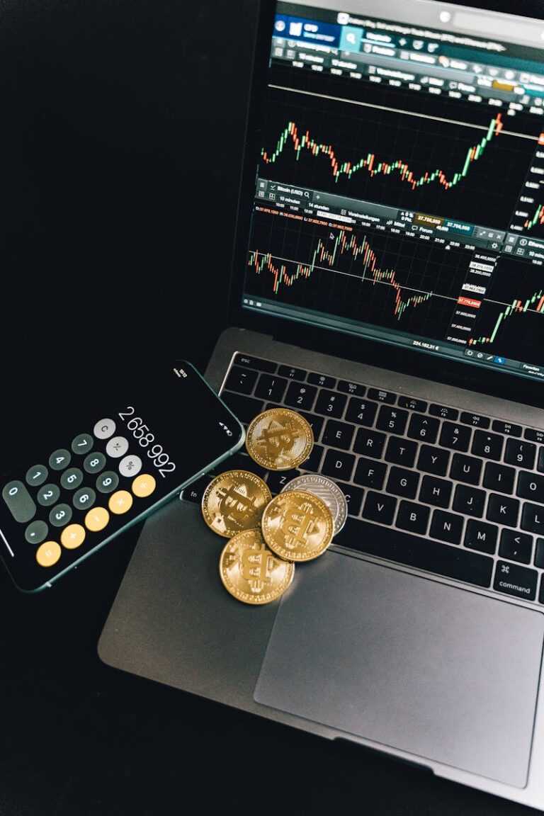 A still life of Bitcoin coins, a smartphone calculator, and a trading chart on a laptop.