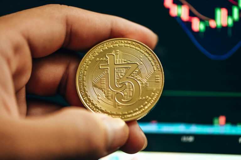 a hand holding a gold bitcoin in front of a stock chart